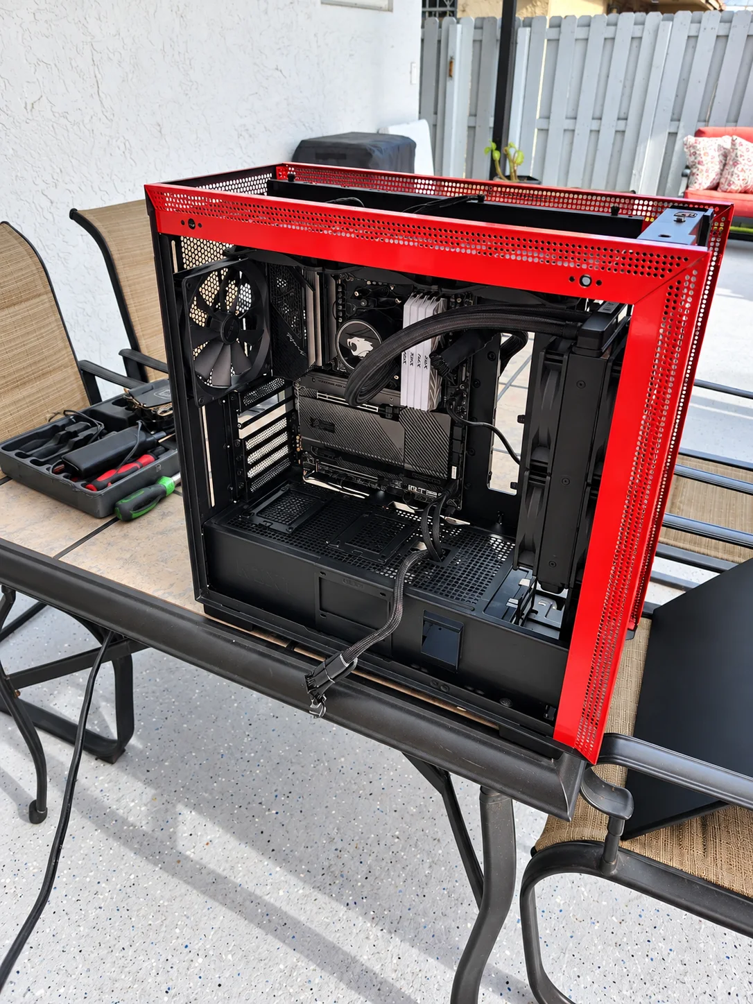 Red PC case with its side panel removed, exposing internal components beside a tool kit.