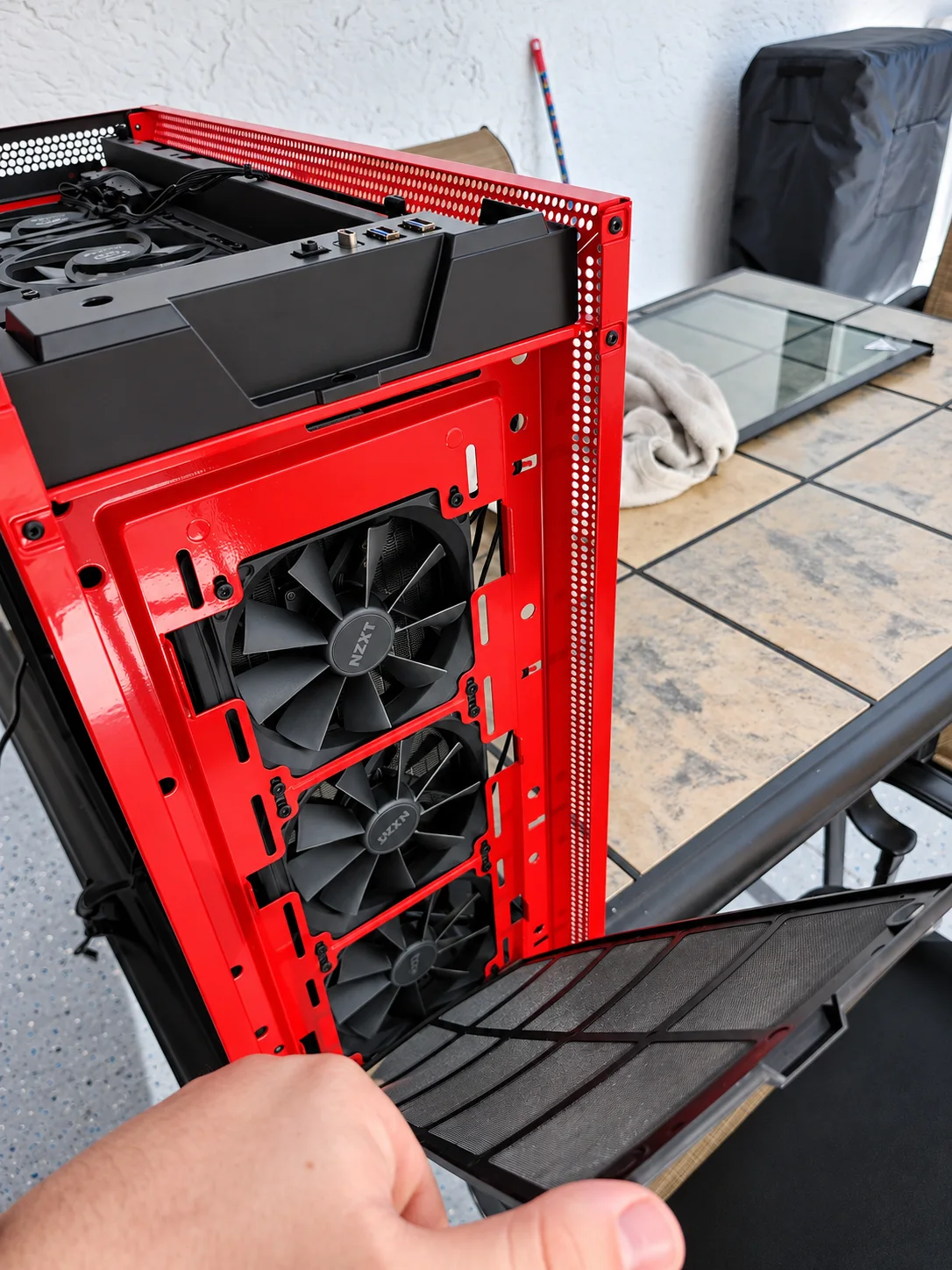 A removable dust filter held in front of three fans in a red PC case.