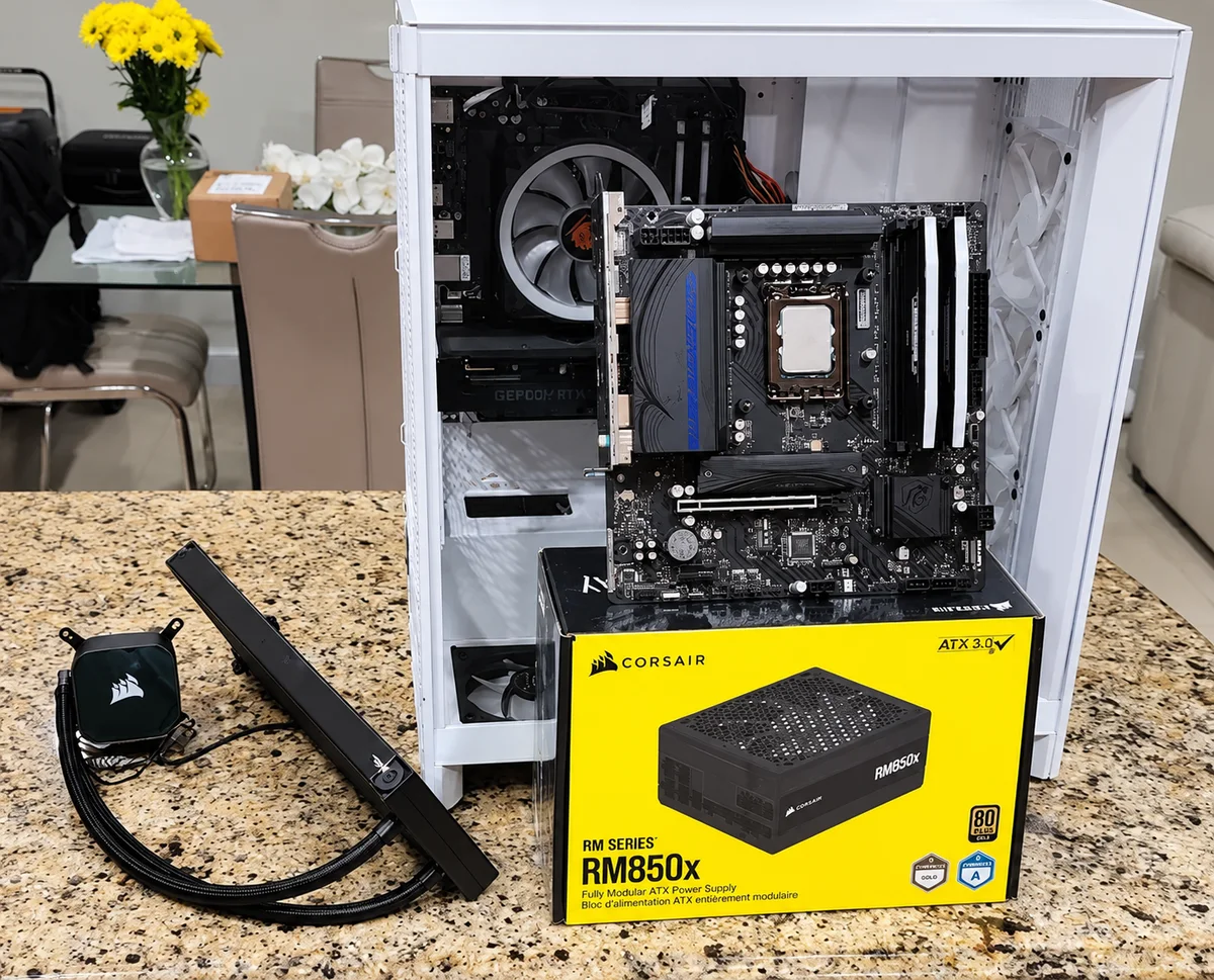 Open white PC case with a motherboard, liquid cooler and boxed power supply on the work surface.